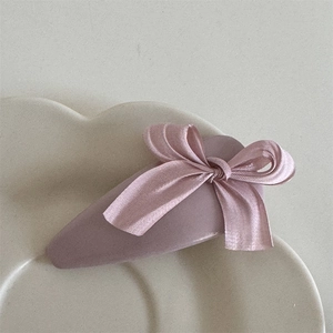 Close-up of a matte mauve fabric bow hair clip on a textured ceramic tray