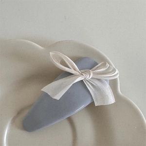 Detailed macro view of a cream satin bow hair clip placed on a white ceramic plate