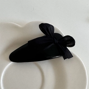 Close-up of elegant black bow hair clip with organza detail on white petal plate