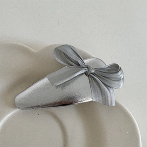 Detail view of a silver ribbon bow hair clip placed on a white petal ceramic tray