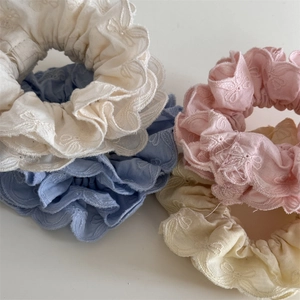 Détail de quatre chouchous pastel avec broderie florale et bords à volants élégants