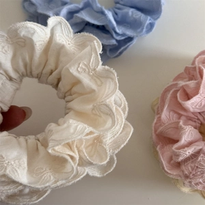 Détail de chouchous en tissu crème, rose et bleu avec broderie florale et noeuds