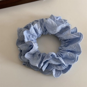 Détail d'un chouchou en dentelle bleu clair avec broderie florale et bord ondulé