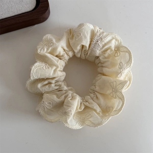 Détail d'un chouchou beige avec bords en dentelle et broderies de nœuds délicats