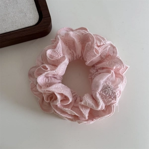 Détail d'un chouchou en dentelle rose pâle avec broderie florale et bords ondulés