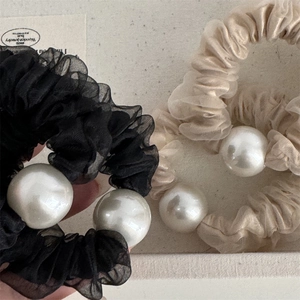 Dettaglio di elastici in organza trasparente con perle oversize nere e champagne