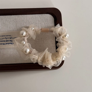 Detail of cream organza hair scrunchie with layered pleats and faux pearl embellishments