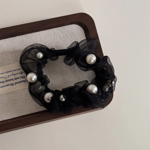 Detailed shot of black organza scrunchie with scattered white faux pearls on linen