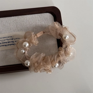 Detail of organza hair scrunchie in champagne with pearls on a linen display