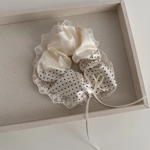 Close-up of cream satin hair scrunchie with lace edges and black polka dot pattern