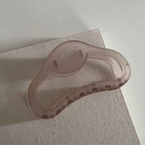 Detail of matte coffee resin hair claw with wavy hollow design on beige canvas