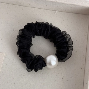 Dettaglio dell'elastico in chiffon plissettato nero con una grande perla bianca decorativa