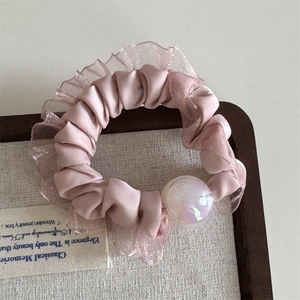 Detail of pink silk scrunchie with lace trim and iridescent pearl on a wooden tray
