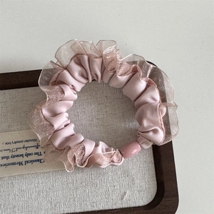 Pink satin scrunchie with pleated lace edge and pearl bead detail on a textured base