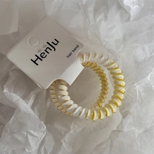 Dettaglio di due elastici a spirale sfumati bianco perla e giallo crema su carta