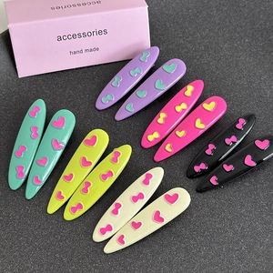 Set of 12 colorful oval hair clips with heart and bow patterns on dark background