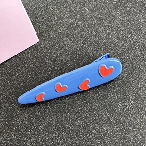 Close-up of sky blue metal hair clip with red heart pattern and smooth lacquer finish