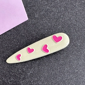 Detail of cream hair clip with pink heart prints on a textured grey surface