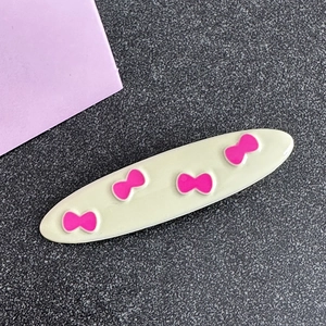 Detail view of a cream hair clip featuring four pink 3D bow accents in a glossy finish