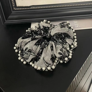 Close-up of white mesh scrunchie with black floral embroidery and pearl trim