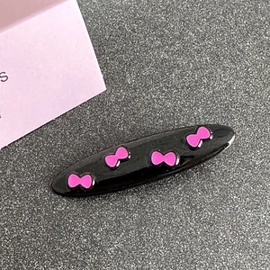 Close-up of black oval hair clip with cute pink bow patterns and glossy finish