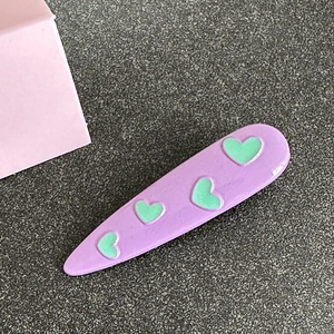 Macro detail of purple teardrop hair clip featuring green heart pattern and smooth finish