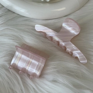 Pink pearlescent acetate hair claw clips with striped texture on soft white fur background