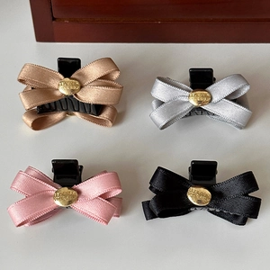 Dettaglio di quattro fermagli per capelli in raso nei colori oro, argento, rosa e nero