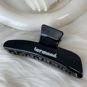 Close-up of black glossy hair claw clip with white larmaad lettering on soft fur background