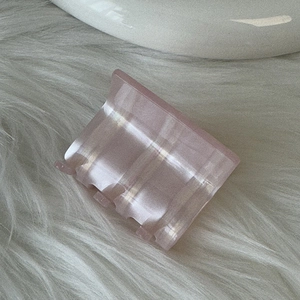 Close-up of a pink acetate hair claw clip with pearlescent texture on a soft plush surface