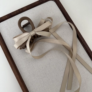 Detail view of champagne ribbon bow with long streamers on a matte brown hair claw clip