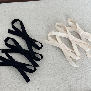 Detailed view of five fabric bow hair clips in black and cream beige on textured fabric