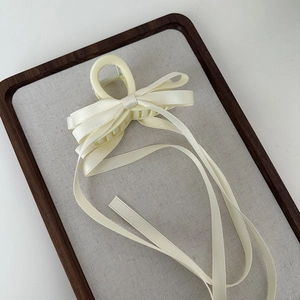 Detail of cream fabric bow hair claw clip with long ribbon streamers on soft fabric tray