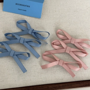 Three handmade fabric bow hair clips in blue and pink on an elegant accessory card