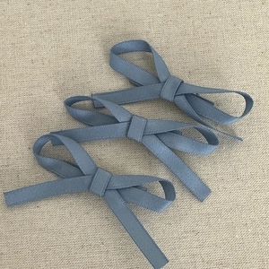 Detailed macro view of three elegant dusty blue silk bow hair clips with ribbed texture
