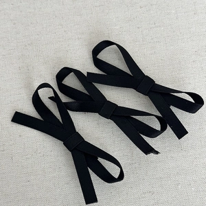 Close-up of three black fabric bow hair clips on a light textured background