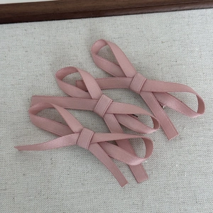 Detailed view of three pink fabric ribbon bow hair clips on a minimalist textured surface