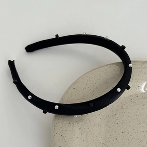 Detailed view of black mercerized headband with white pearls and square studs on ceramic