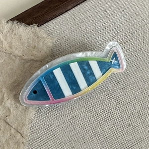 Detail einer fischförmigen Haarspange mit blauen Streifen und Regenbogen-Glitzer