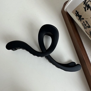 Detailed view of large matte black shark hair claw clip with elegant crossed wave design