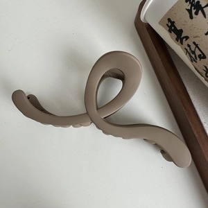 Close-up of matte coffee brown wavy shark hair claw clip on a minimalist white desk