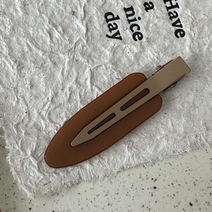 Detail of matte brown and beige duckbill hair clip on a textured paper background