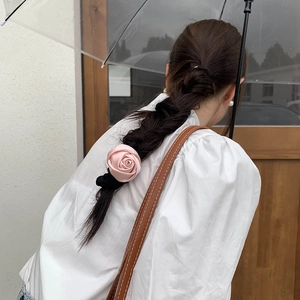 Pink satin rose hair scrunchie detail showing floral texture on a dark braided hairstyle