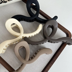 Set of four matte large hair claw clips in neutral tones on a stylish wooden display tray