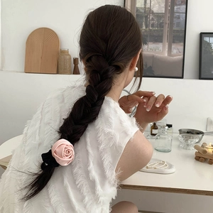 Detail view of a soft pink satin rose hair scrunchie worn on hair in a cozy home setting
