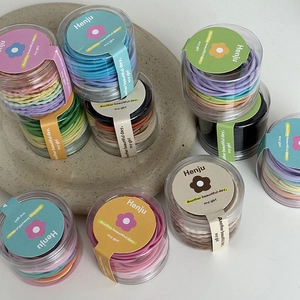 Colorful high elasticity hair ties in a clear cylindrical jar on a ceramic tray