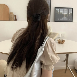 Detail of 3D satin black rose hair scrunchie styled on long hair in a cozy indoor setting