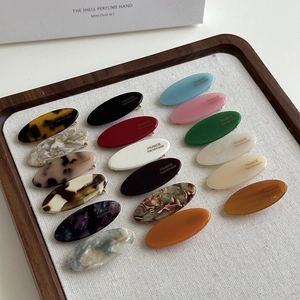 Flat lay of 18 colorful acetate oval hair clips in a wooden tray showing diverse marble textures