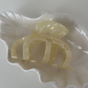 Détail de la pince à cheveux en acétate crème avec logo doré dans un plat en céramique