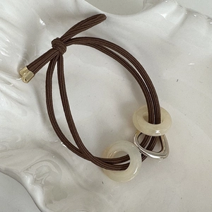 Détail d'un élastique marron avec des anneaux en résine et un pendentif coeur argent